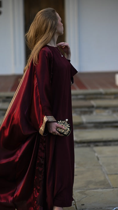 Person wearing a burgundy abaya with a gold trim sleeve.