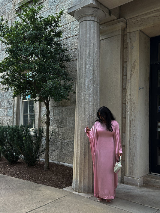 Woman in a pink dress standing next to a stone column outdoors.