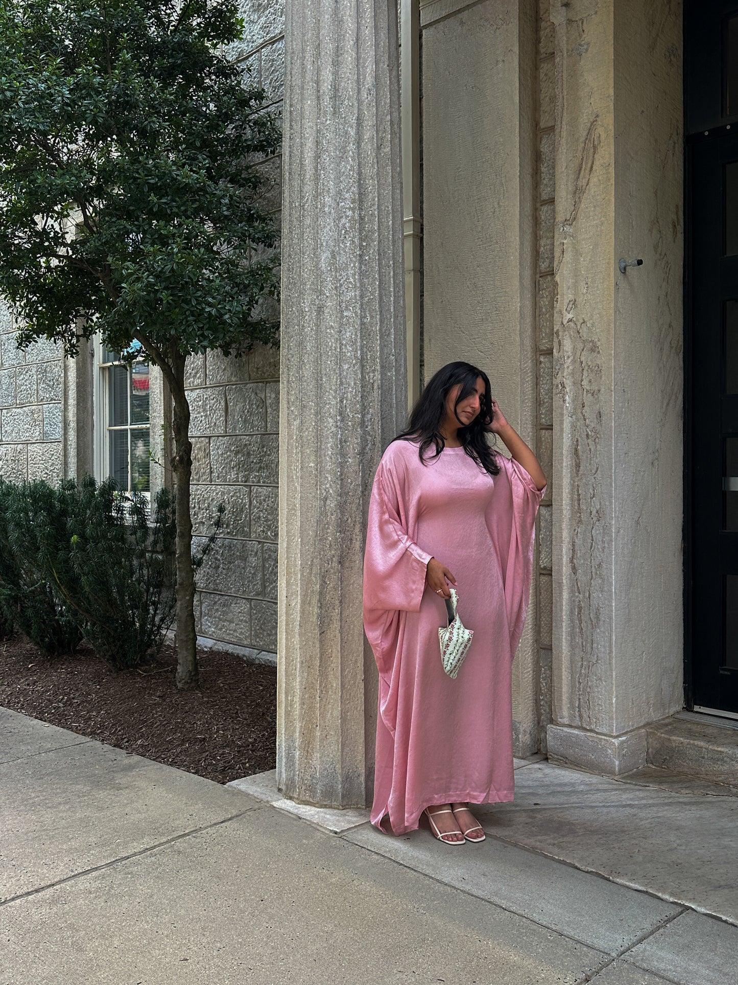 Woman in a pink dress standing next to a stone building