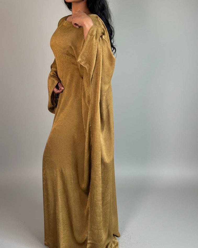 Woman wearing a long, flowing mustard yellow abaya against a plain background
