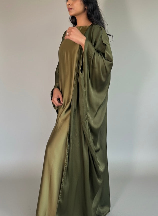 Woman wearing a long olive green satin dress against a plain background