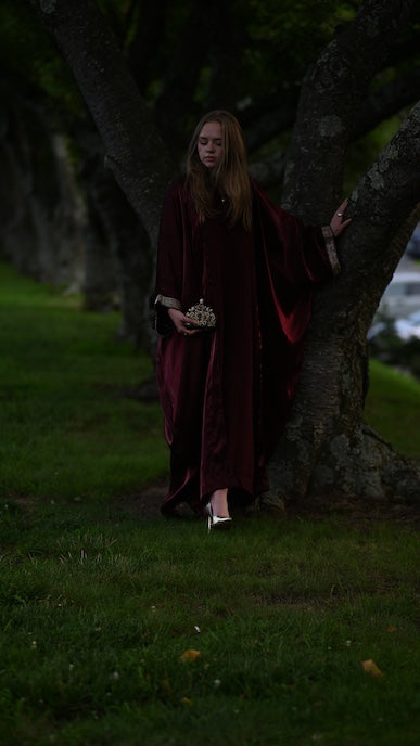 Person wearing a burgundy abaya with a gold trim sleeve.