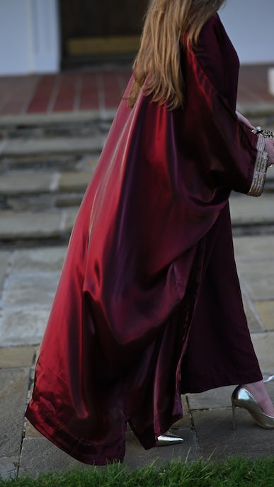 Person wearing a burgundy abaya with a gold trim sleeve.