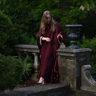 Person wearing a burgundy abaya with a gold trim sleeve.