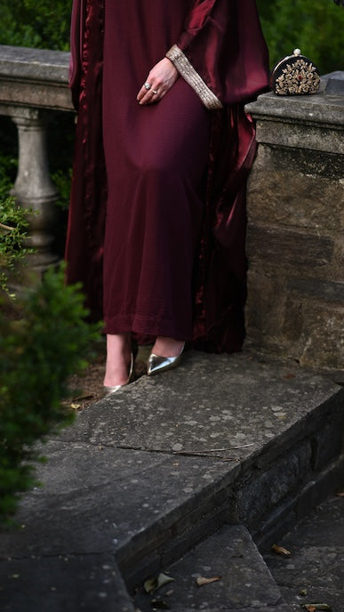 Person wearing a burgundy abaya with a gold trim sleeve.
