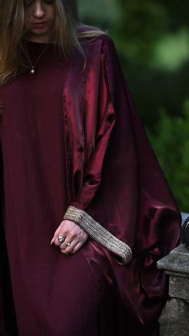Person wearing a burgundy abaya with a gold trim sleeve.