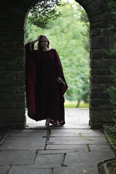 Person wearing a burgundy abaya with a gold trim sleeve.