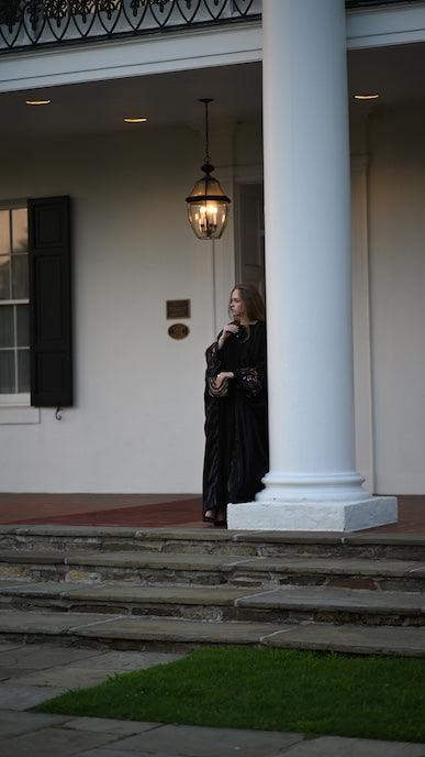 Woman in a black abaya standing on a staircase in front of a white house with columns.