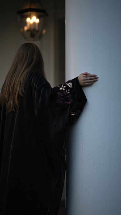 Person in a dark abaya leaning against a light blue wall with a chandelier in the background.