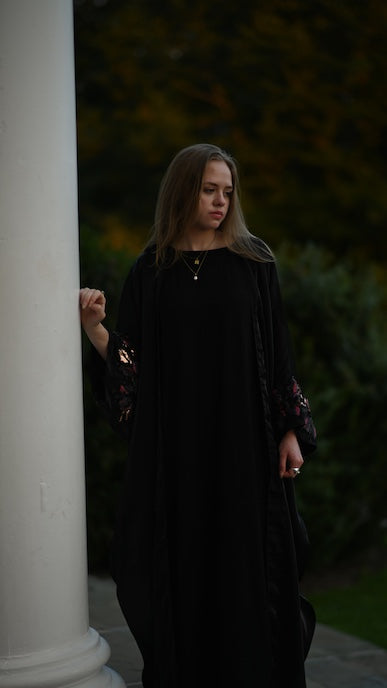 Woman in a dark abaya standing next to a white column with a blurred background