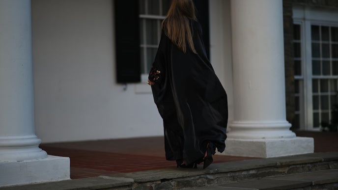 Person in a long black abay walking on a stone path with classical columns in the background