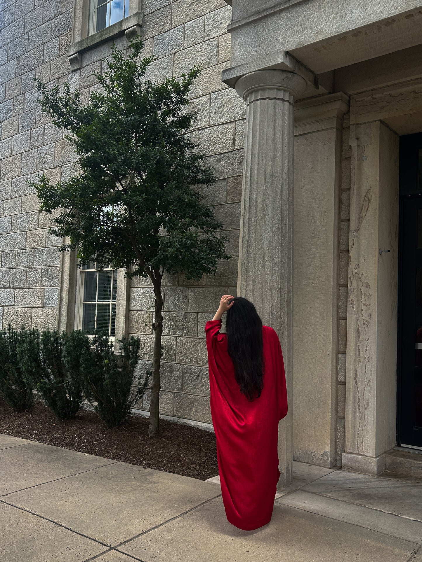 Person in a red abaya standing in front of a stone building with columns.