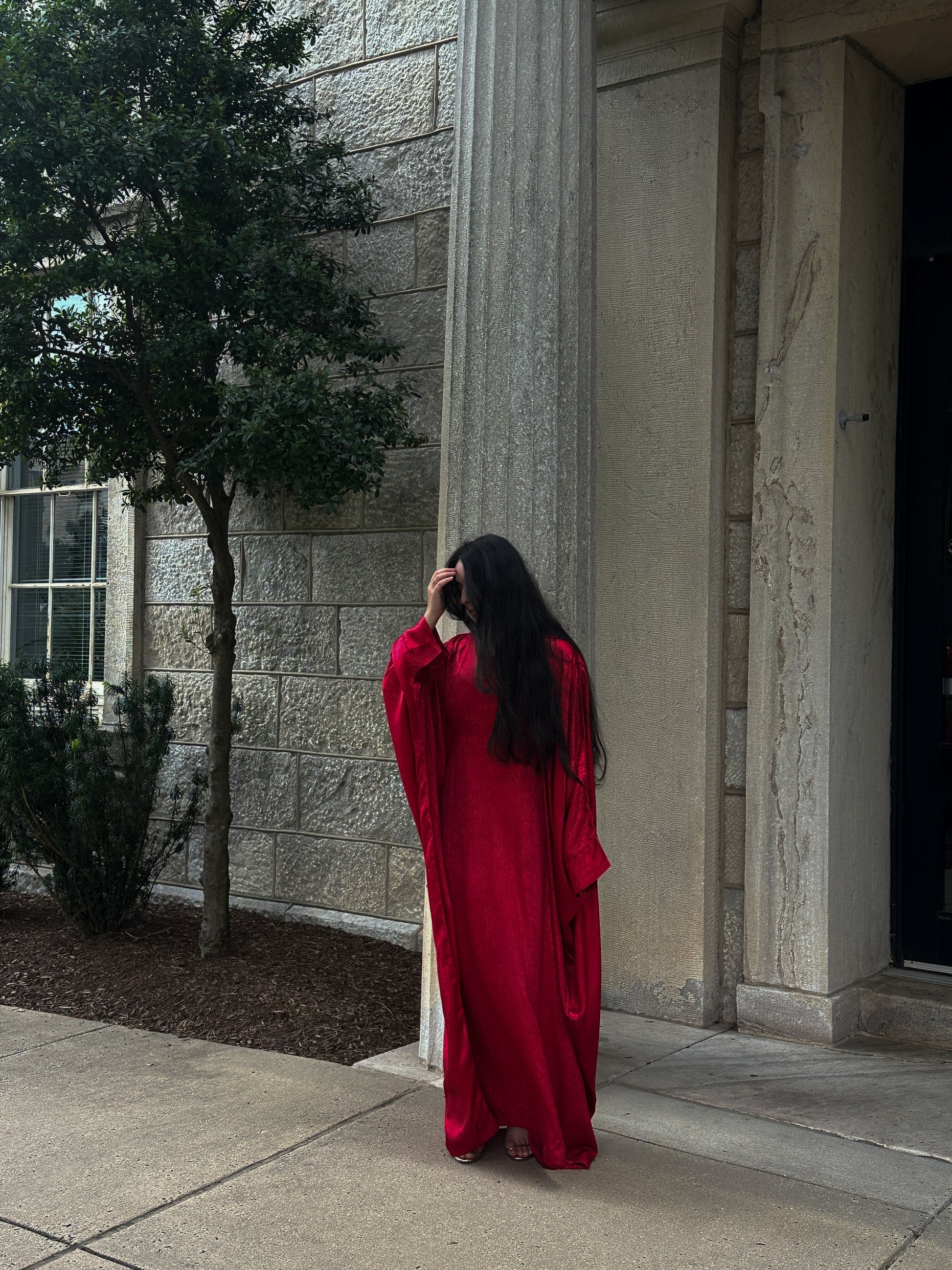 Person in a red abaya standing outside a building with columns