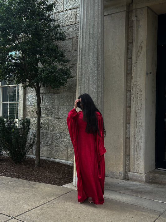 Person in a red abaya standing outside a building with columns