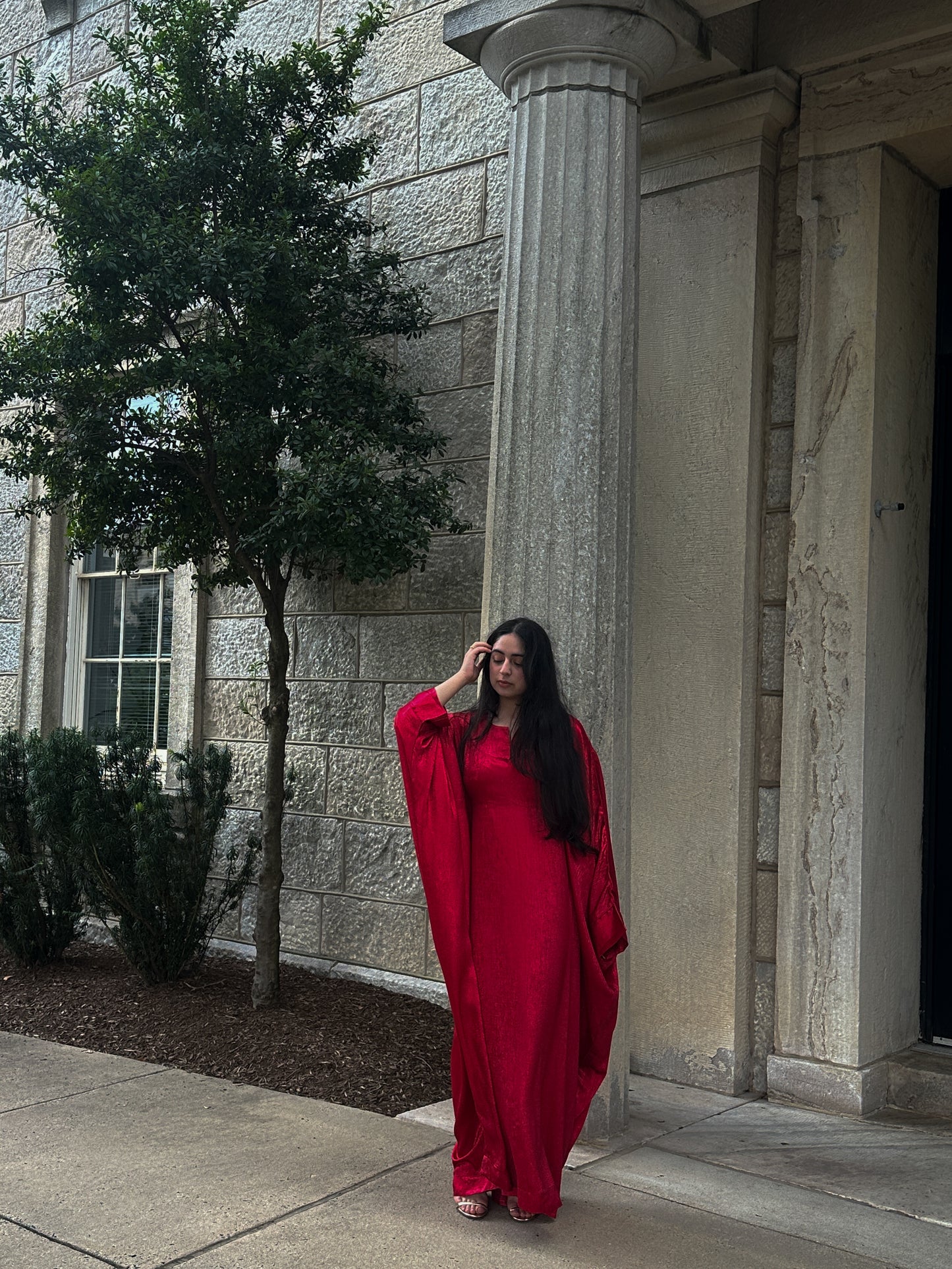 Woman in a red abaya standing against a stone building with columns.