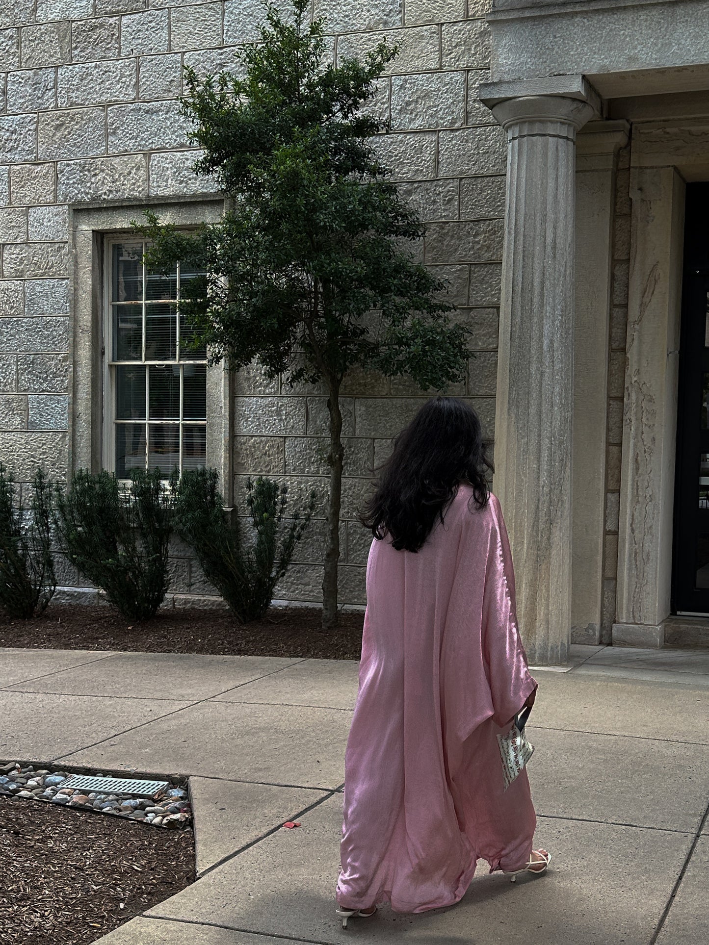 Person in a pink dress walking past a stone building with columns