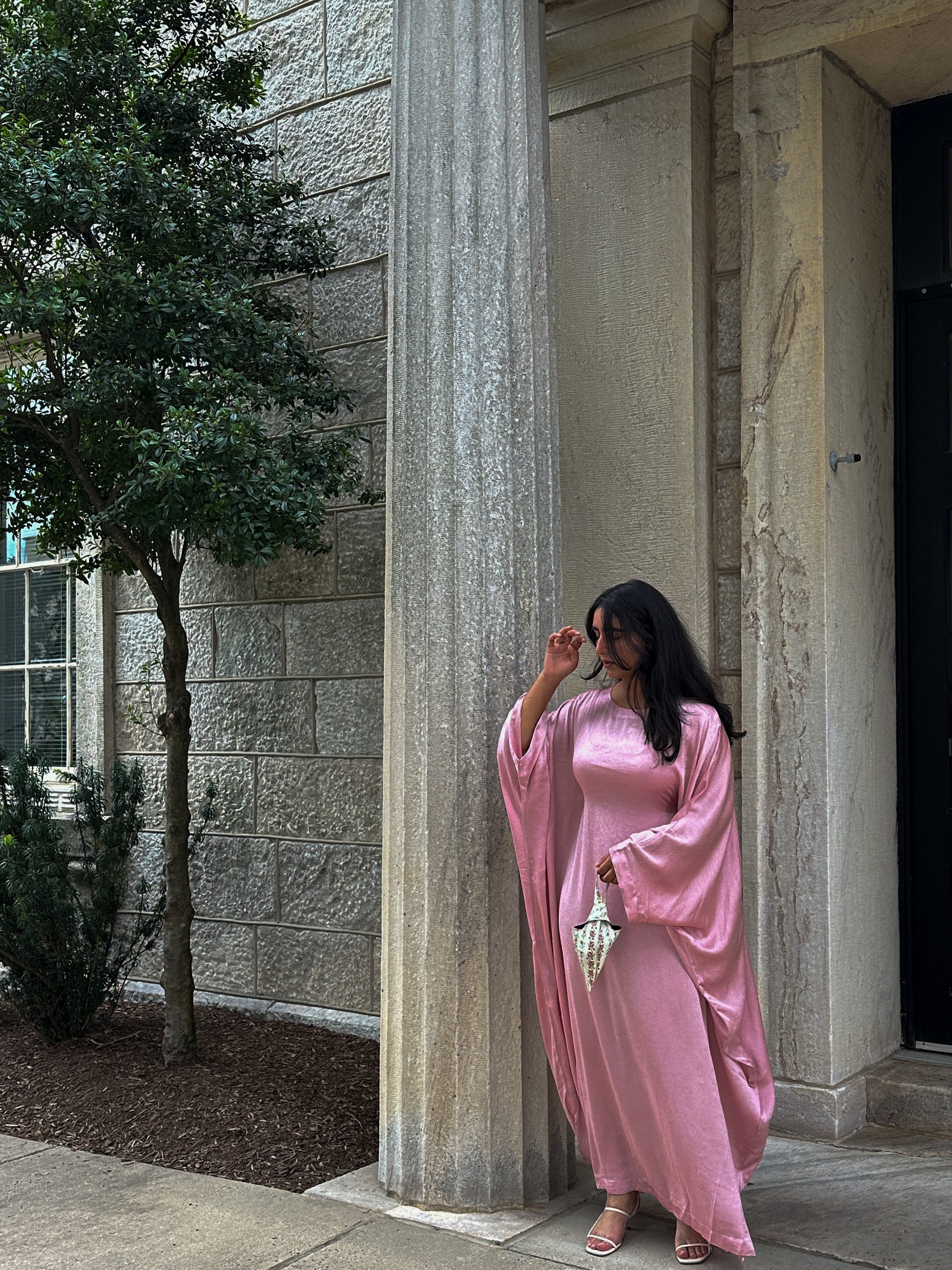 Woman in a pink dress standing next to stone columns outdoors
