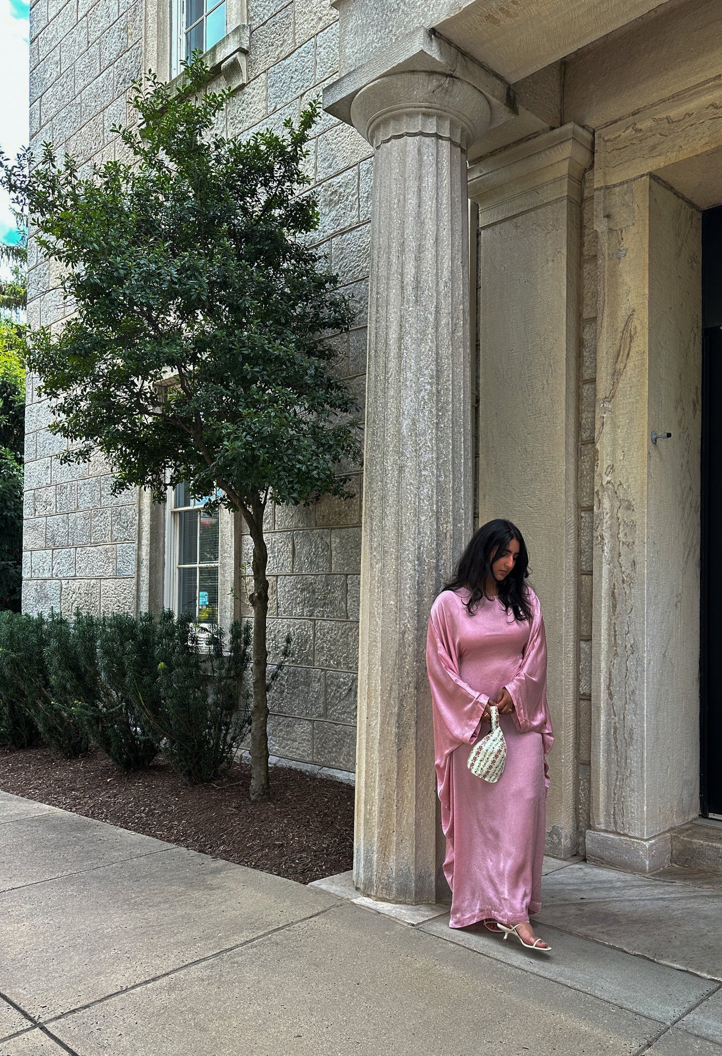 Woman in a pink dress standing in front of a stone building with columns.