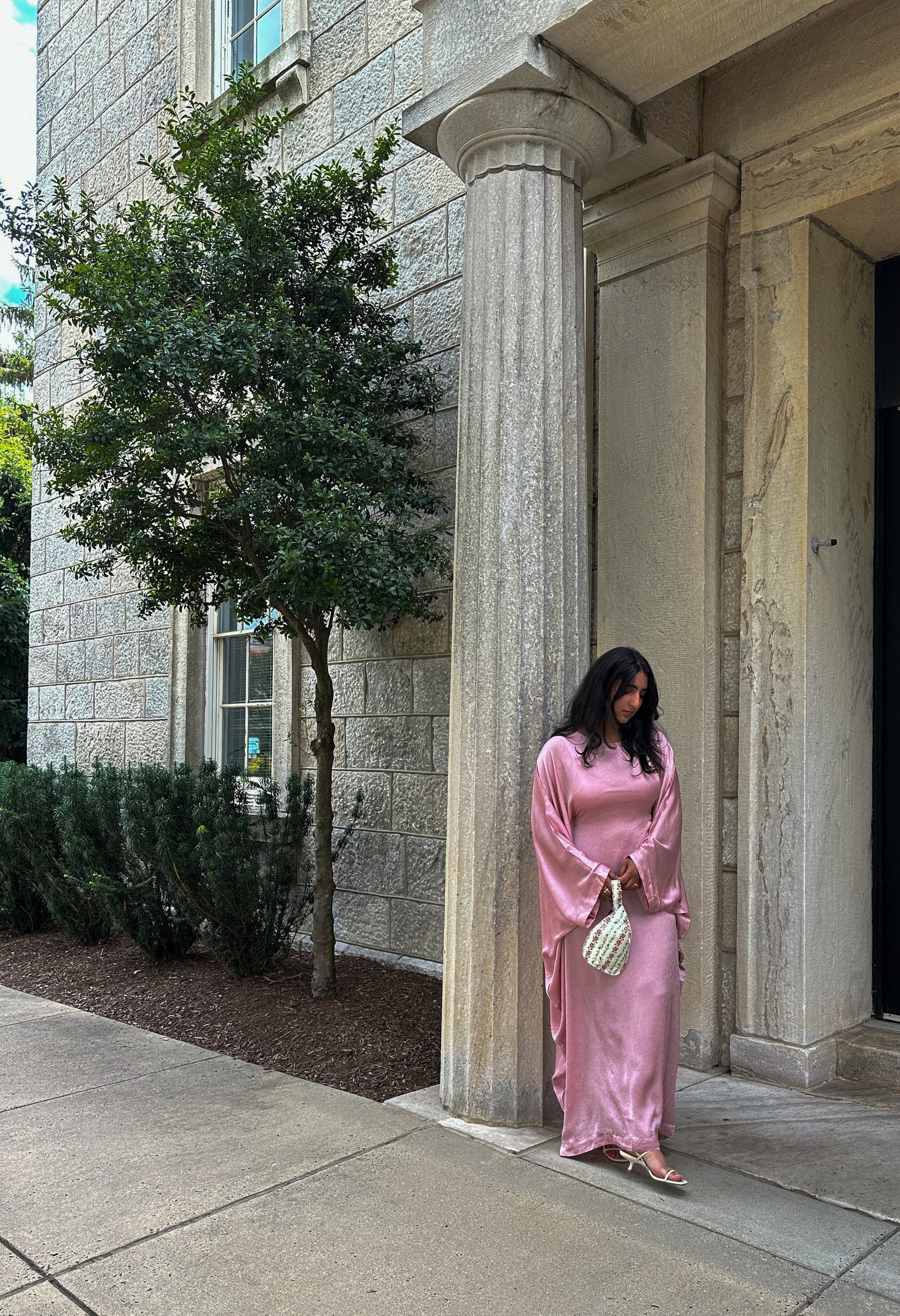 Woman in a pink dress standing in front of a stone building with columns.