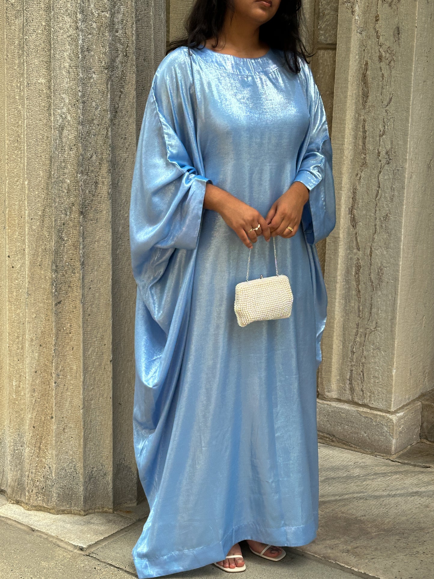 Woman wearing a light blue dress standing against a stone wall.