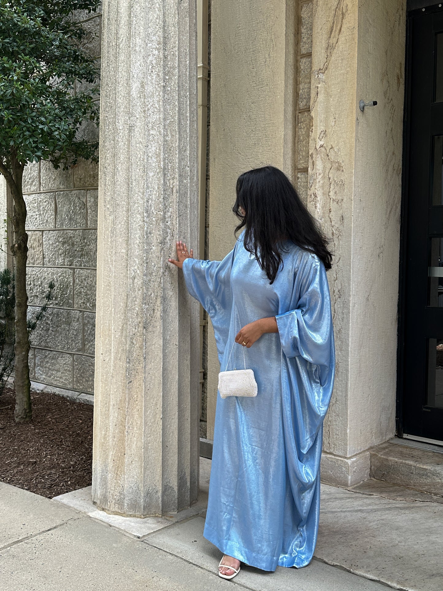 Woman in a light blue dress standing next to a stone column outdoors.