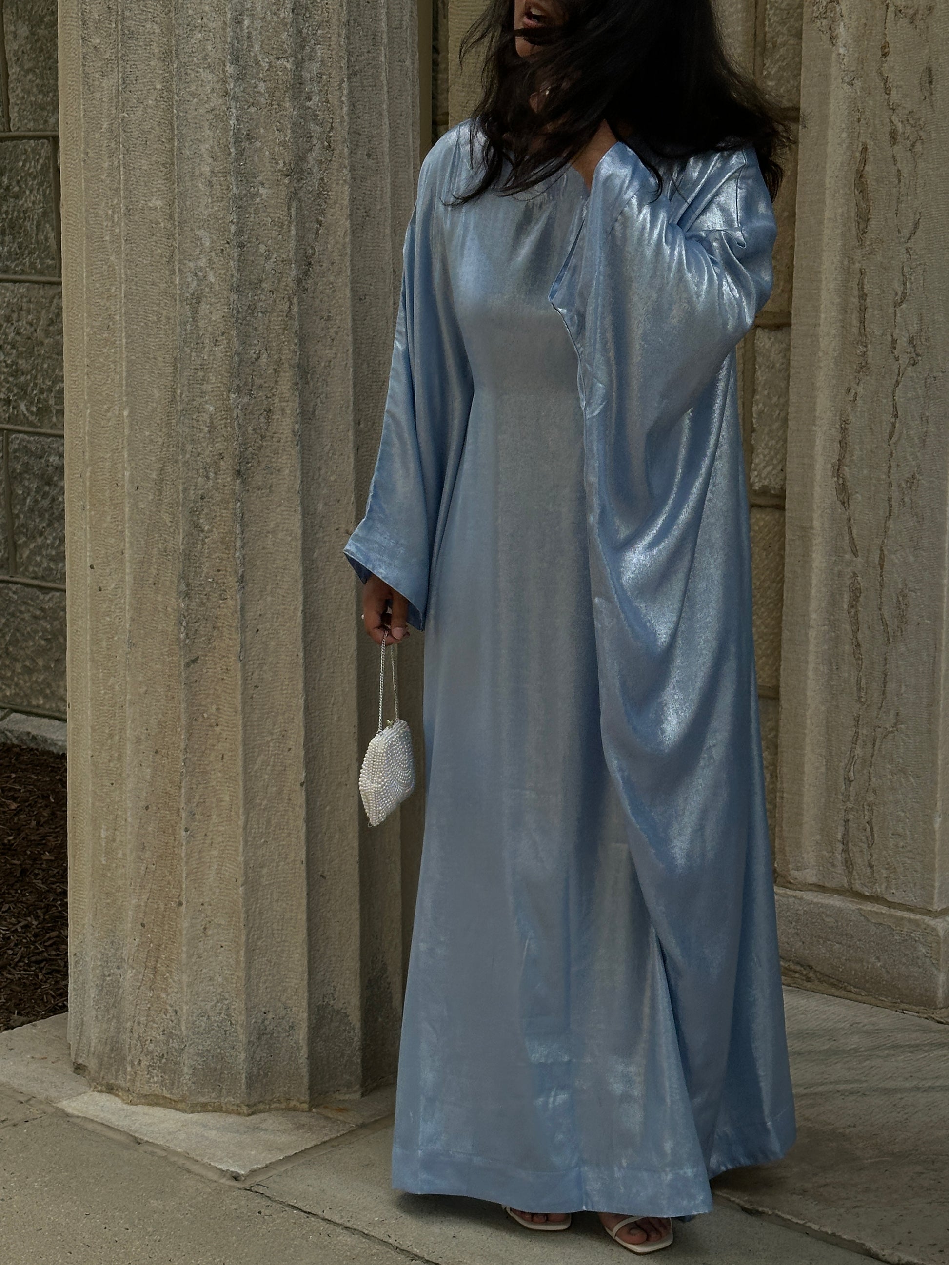 Person wearing a long, shiny blue dress standing on stone steps.