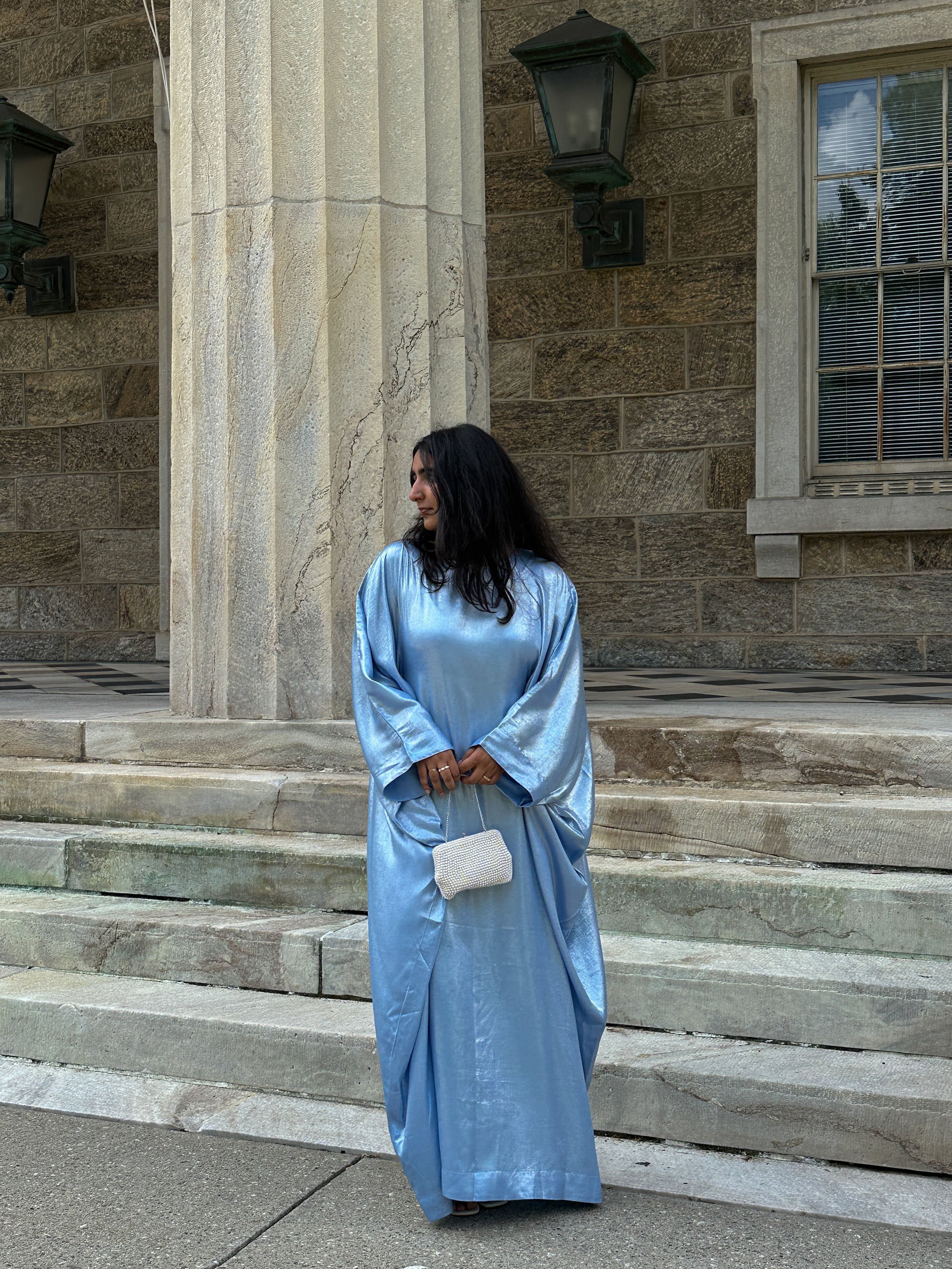 Woman in a blue dress standing on stone steps in front of a stone building.