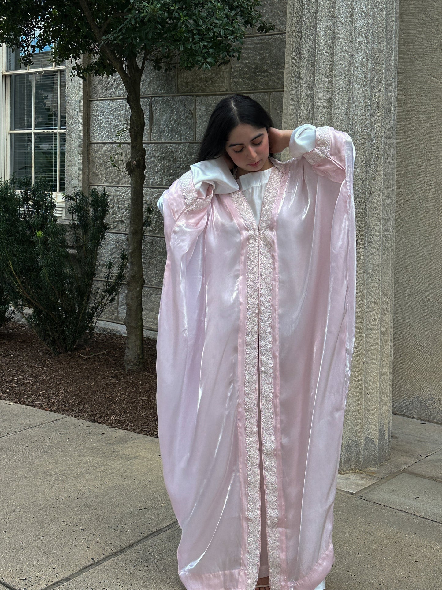 Person wearing a light pink dress with ruffled sleeves and a long train, standing outdoors near a building.
