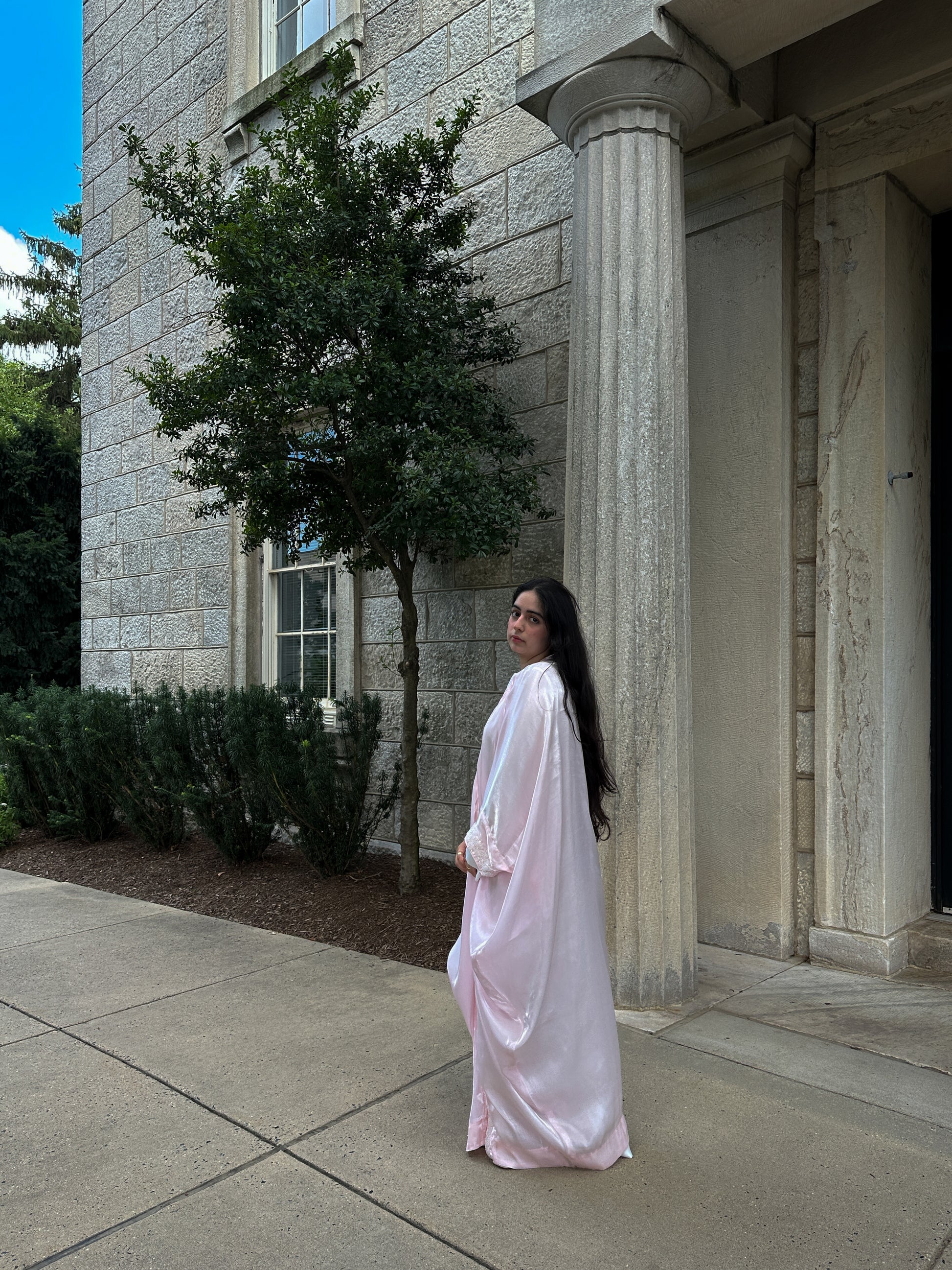 Woman in a white dress standing in front of a stone building with columns.