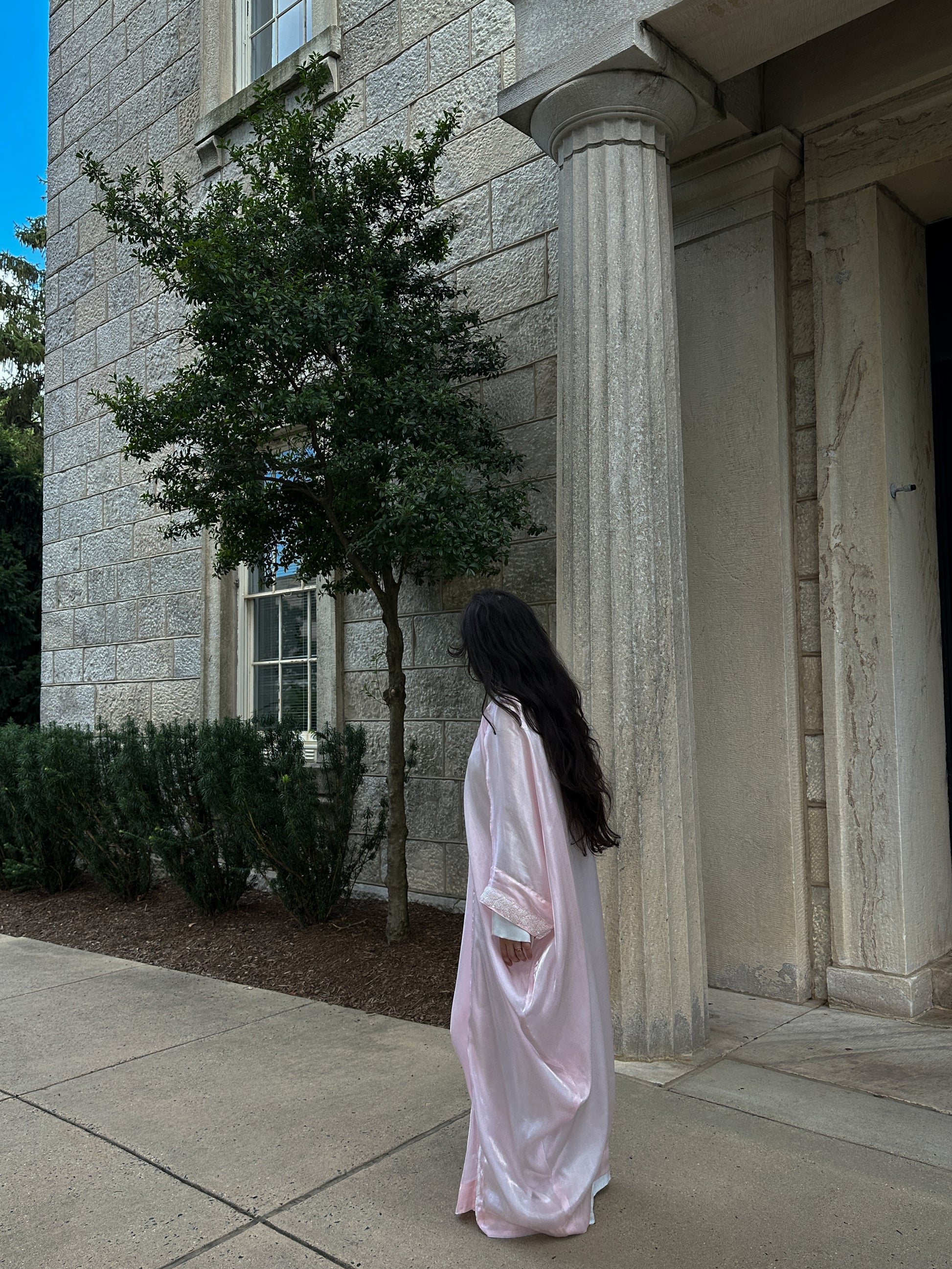 Person in a pink dress standing in front of a stone building with columns.