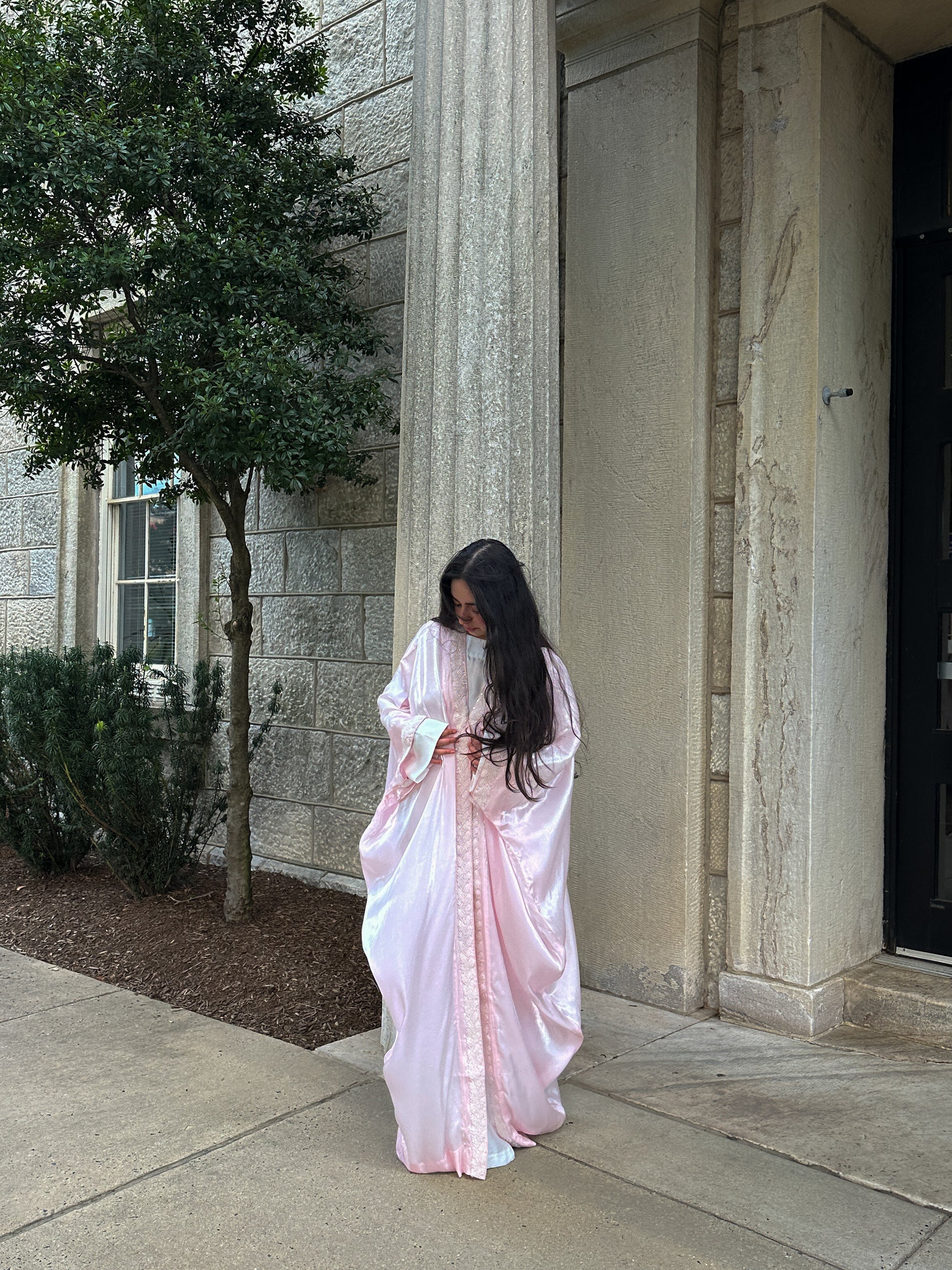 Woman in a pink saree standing outside a building with columns