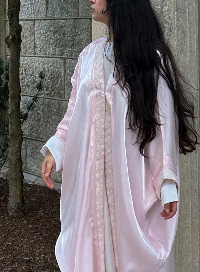 Woman in a light pink dress standing outdoors against a stone wall.