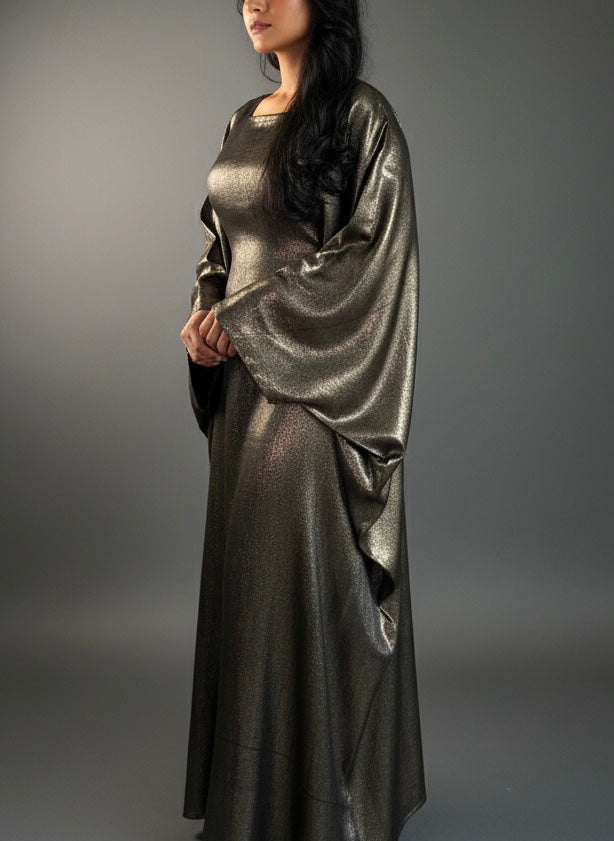 Woman wearing a metallic golden silver  abaya against a gray background