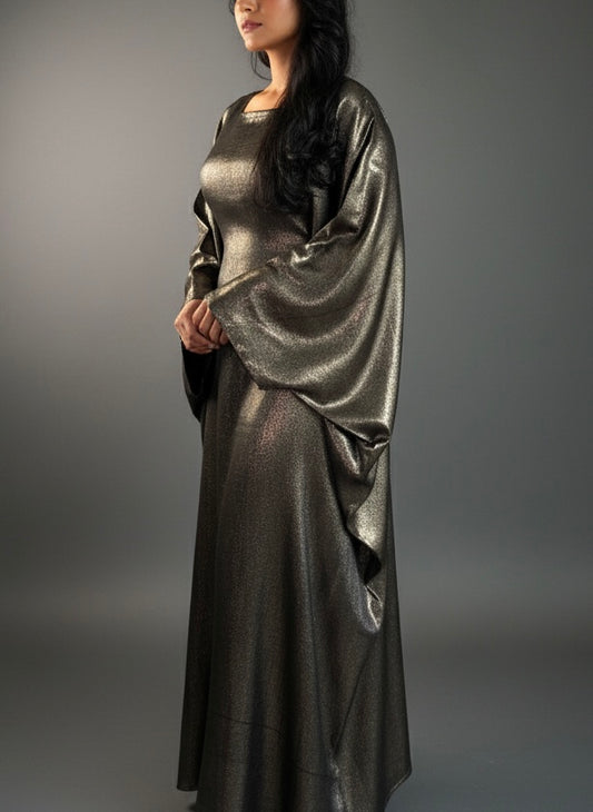 Woman wearing a metallic golden silver  abaya against a gray background