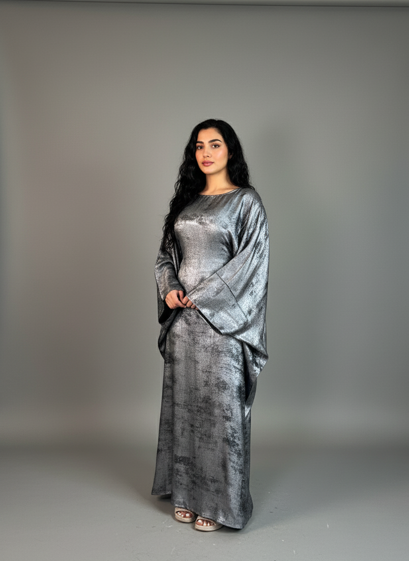 Woman wearing a long, flowing grey shimmery abaya against a plain background
