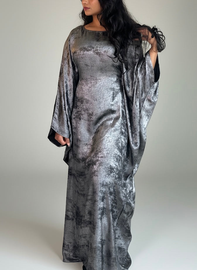 Woman wearing a silver patterned abaya on a plain background