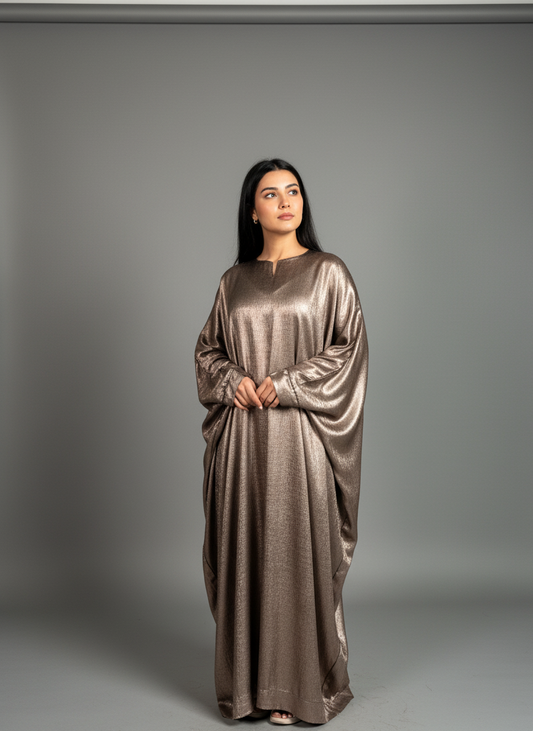 Woman wearing a long, metallic bronze abaya against a gray background