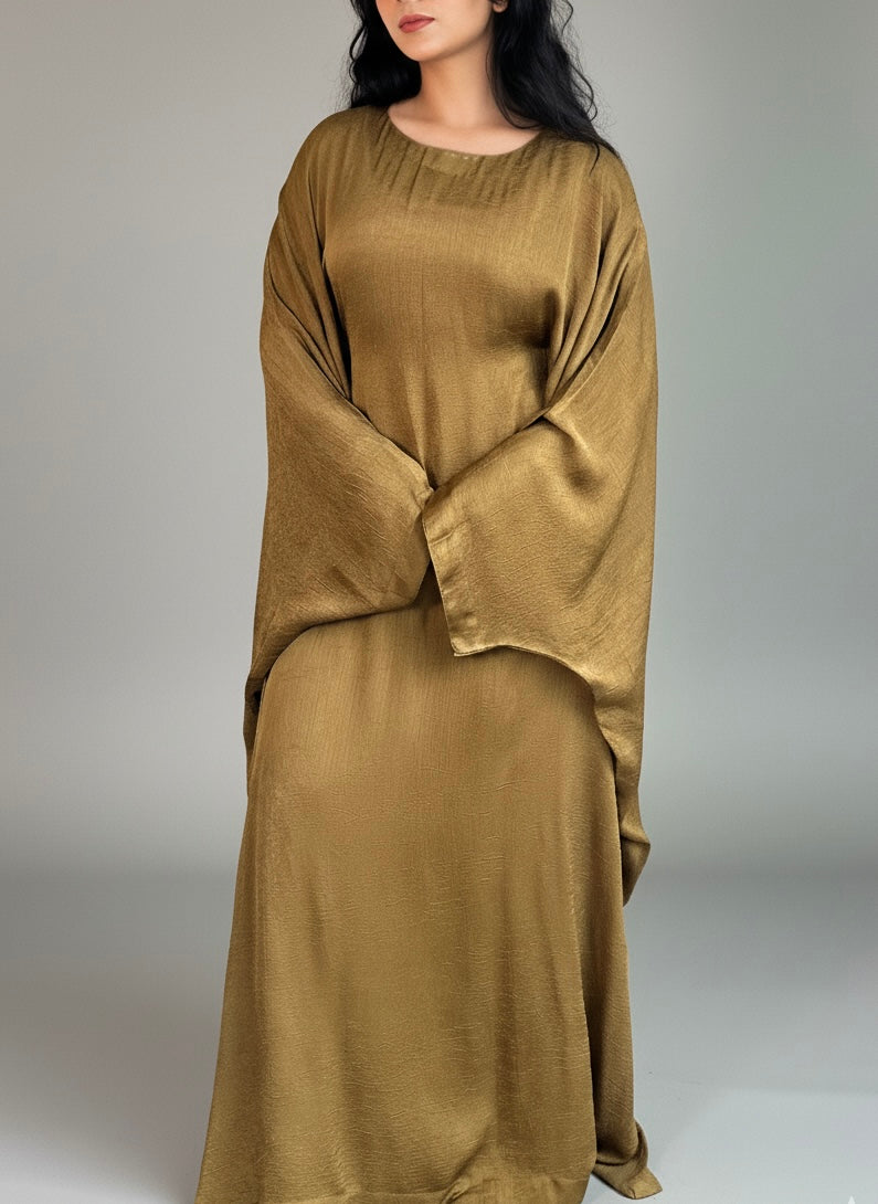 Woman wearing a long, mustard yellow abaya against a plain background