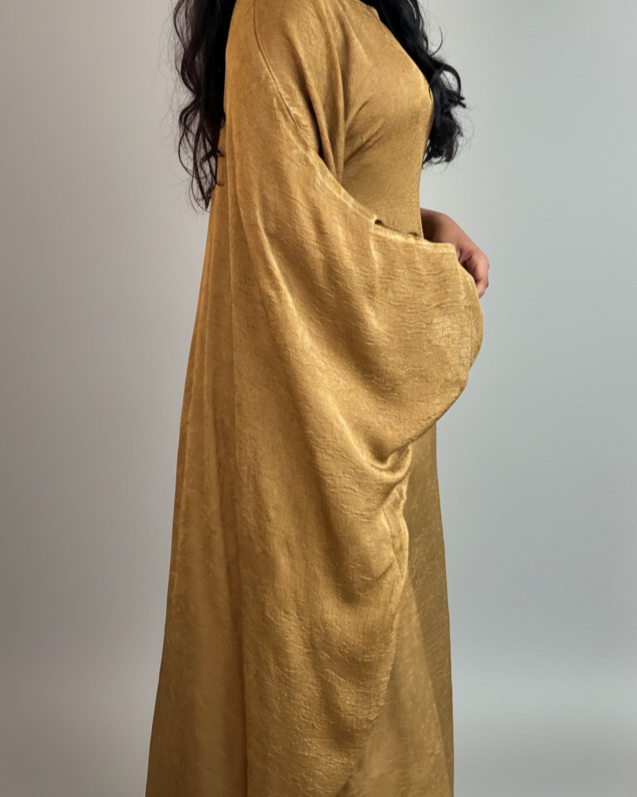 Woman wearing a mustard yellow long-sleeve abaya against a plain background