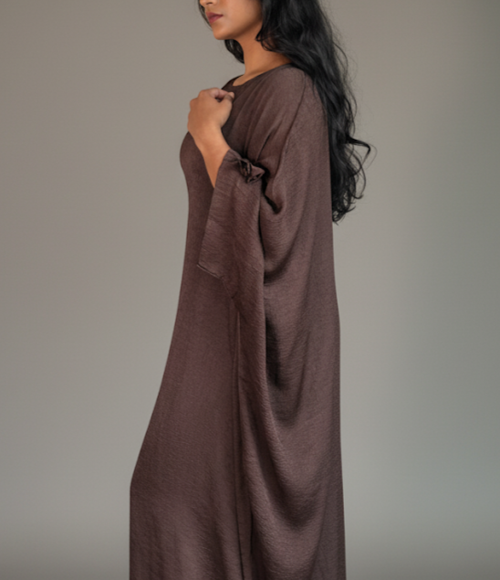 Woman wearing a long brown abaya against a plain background