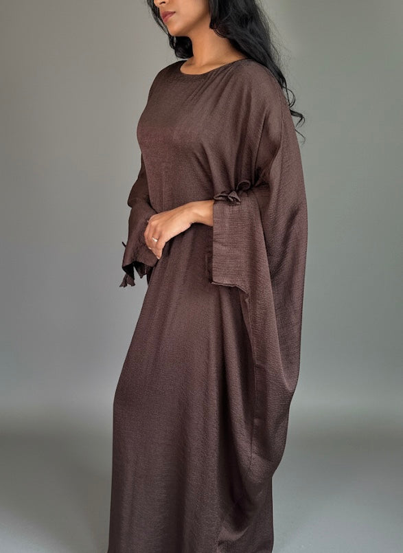 Woman wearing a brown abaya against a plain background