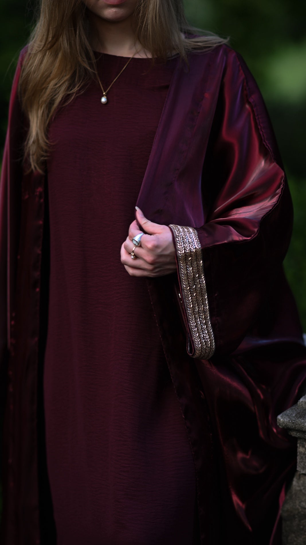 Person wearing a burgundy abaya with a gold trim sleeve.