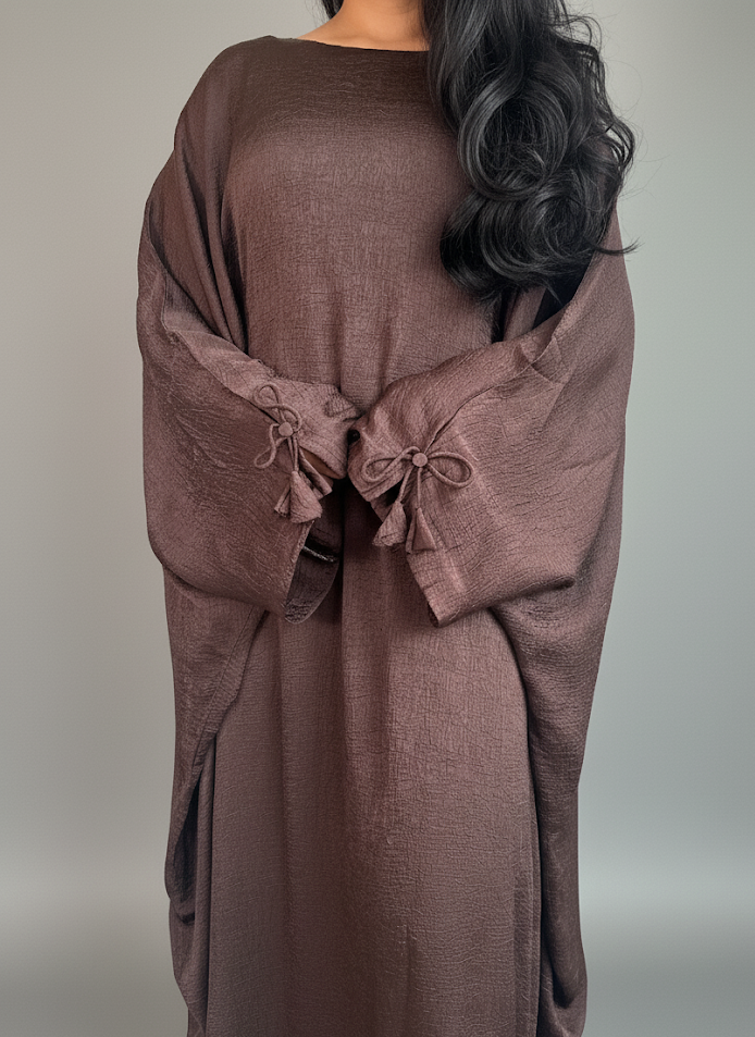 Brown abaya with bow details draped over a person on a neutral background