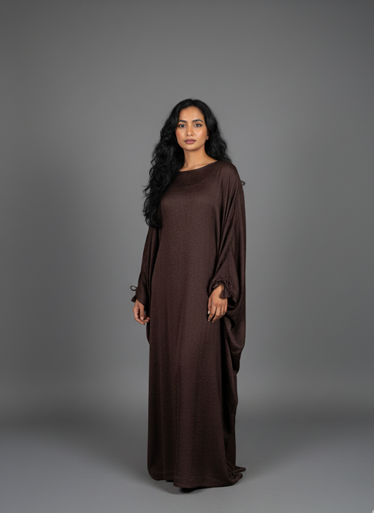 Woman wearing a brown long abaya against a gray background